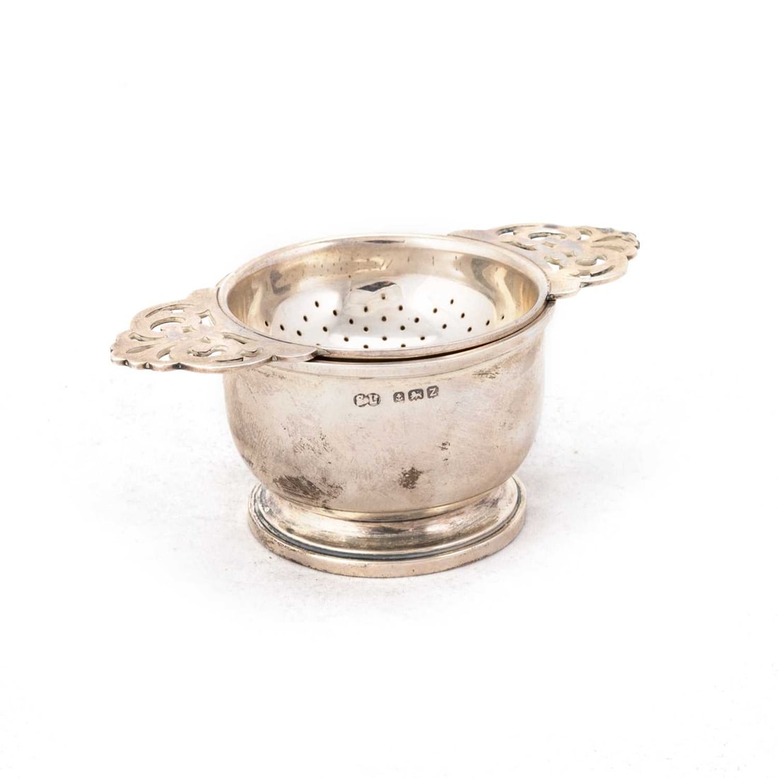 A GEORGE VI SILVER TEA STRAINER ON STAND: A GEORGE VI SILVER TEA STRAINER ON STAND by William Suckling Ltd, Birmingham 1949 and 1950. (2) 10cm across handles, 1.9 troy ounces gross