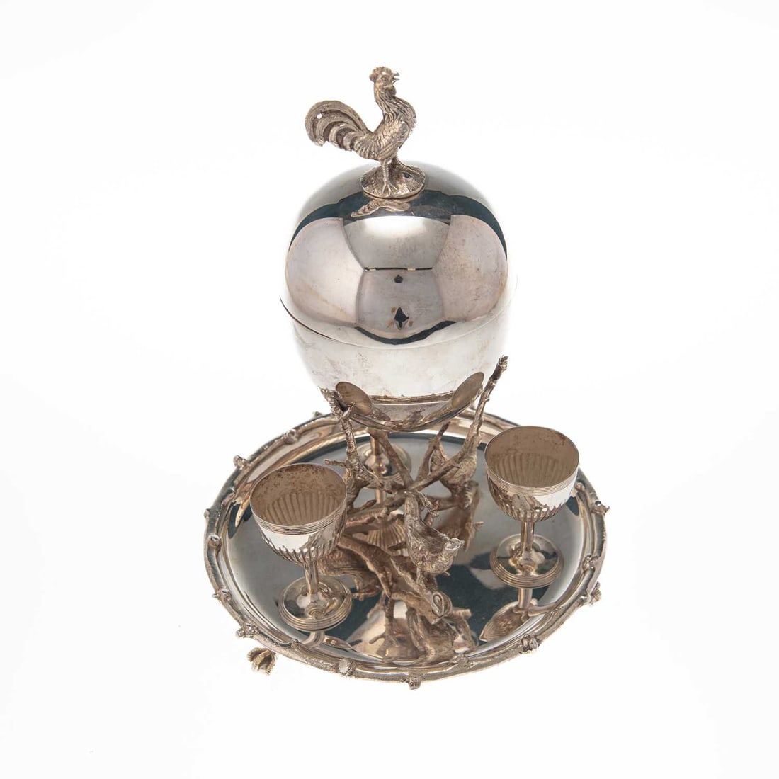 A SILVER-PLATED EGG CODDLER AND CUPS: A SILVER-PLATED EGG CODDLER AND CUPS late 19th/ early 20th Century, egg-shaped with a chicken finial, raised on three branch form supports above a shaped circular base holding three egg cups. 27cm hig