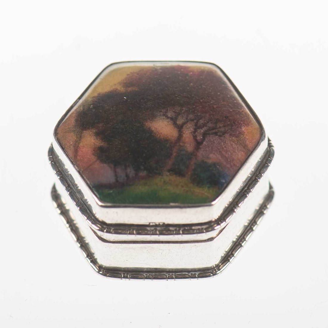 A GEORGE V SILVER AND ENAMEL PILL BOX IN THE MANNER OF CHARLES FLEETWOOD VARLEY (1863-1942): A GEORGE V SILVER AND ENAMEL PILL BOX IN THE MANNER OF CHARLES FLEETWOOD VARLEY (1863-1942) by G.W. Lewis & Co, Birmingham 1923, of hexagonal form, the hinged cover enamel decorated with trees in