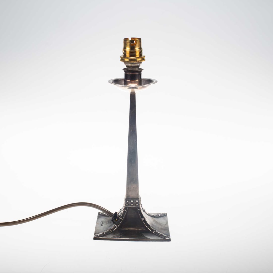 AN ARTS AND CRAFTS SILVER CANDLESTICK LAMP: AN ARTS AND CRAFTS SILVER CANDLESTICK LAMP by John Dixon & Sons Ltd, Sheffield 1904, the sconce of cylindrical form above a circular drip tray, the stem of square section spreading into a large sq