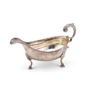 A GEORGE III SILVER SAUCEBOAT: A GEORGE III SILVER SAUCEBOAT by Hester Bateman, London 1784, with a beaded rim and flying scroll handle with an acanthus leaf thumbpiece, engraved to the underside with initials, all raised on three