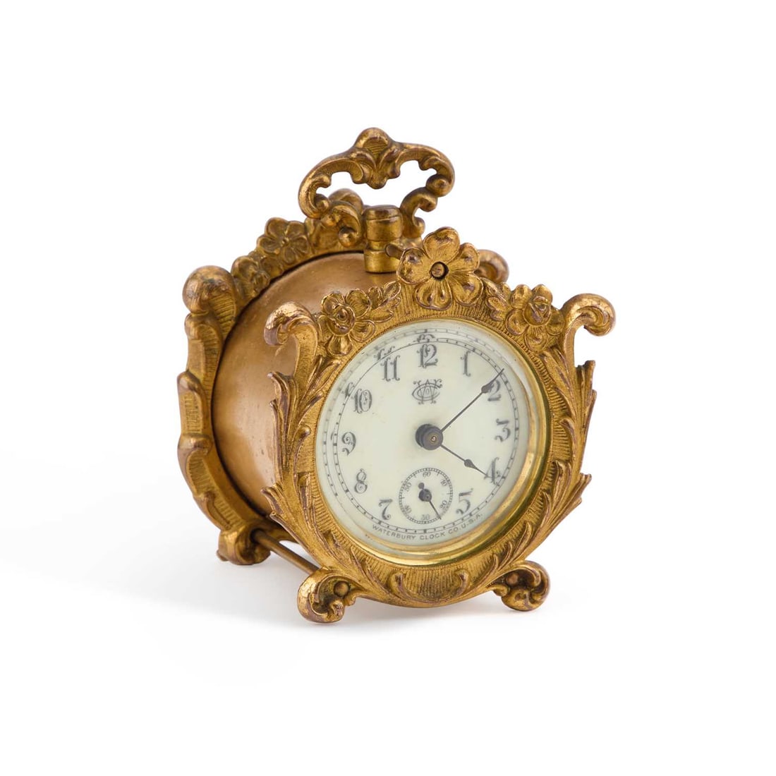 AN AMERICAN GILT-BRASS CLOCK, BY WATERBURY CLOCK CO, EARLY 20TH CENTURY: AN AMERICAN GILT-BRASS CLOCK, BY WATERBURY CLOCK CO, EARLY 20TH CENTURY the circular dial with subsidiary seconds, the drum case with a scroll-cast front and a carrying handle. 9cm high The dial is i