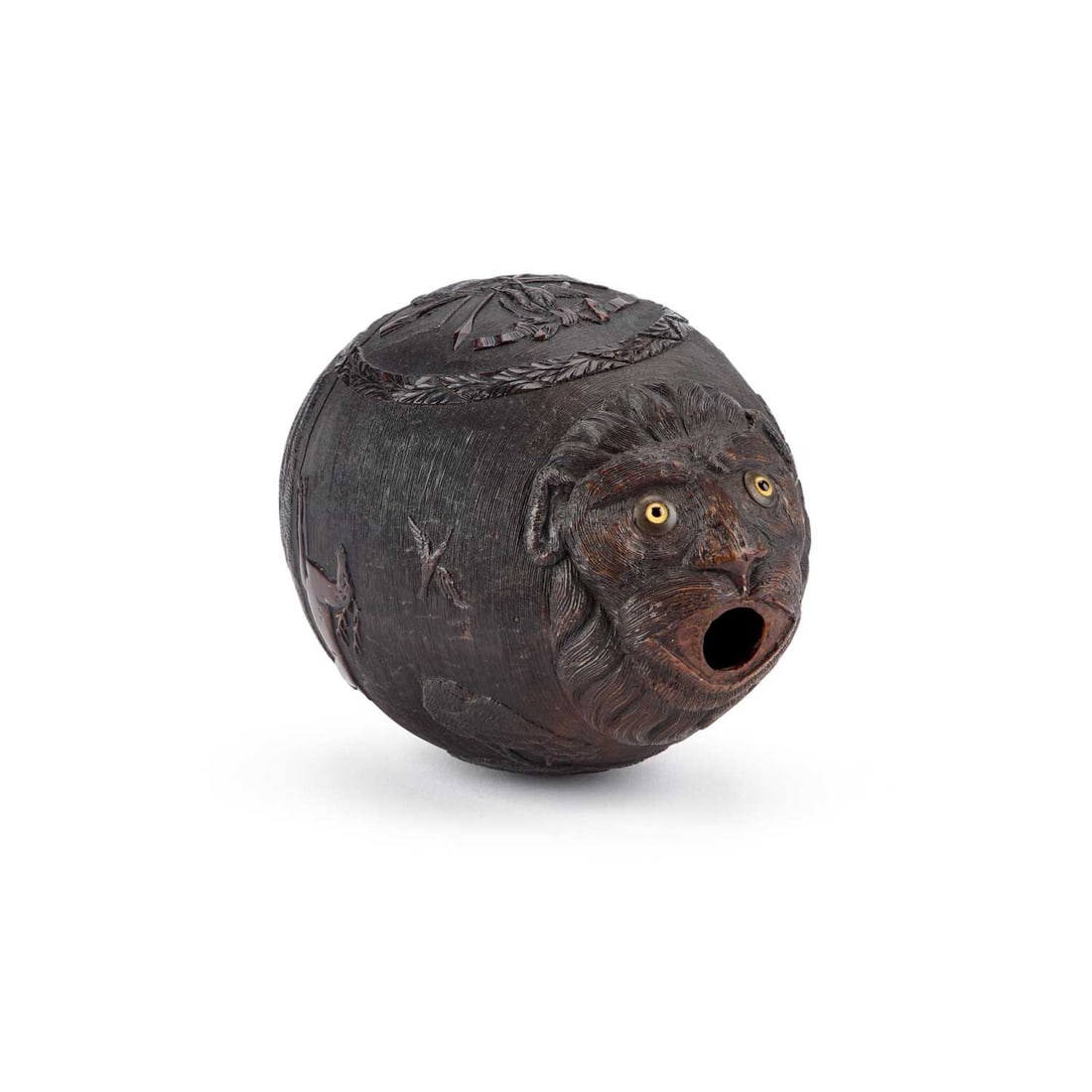 AN 18TH CENTURY CARVED COCONUT: AN 18TH CENTURY CARVED COCONUT with a lion mask to the top inset with glass eyes, above a hunting scene and coat of arms within a wreath, a circular floral pediment at the base. 13.5cm high Possibly a