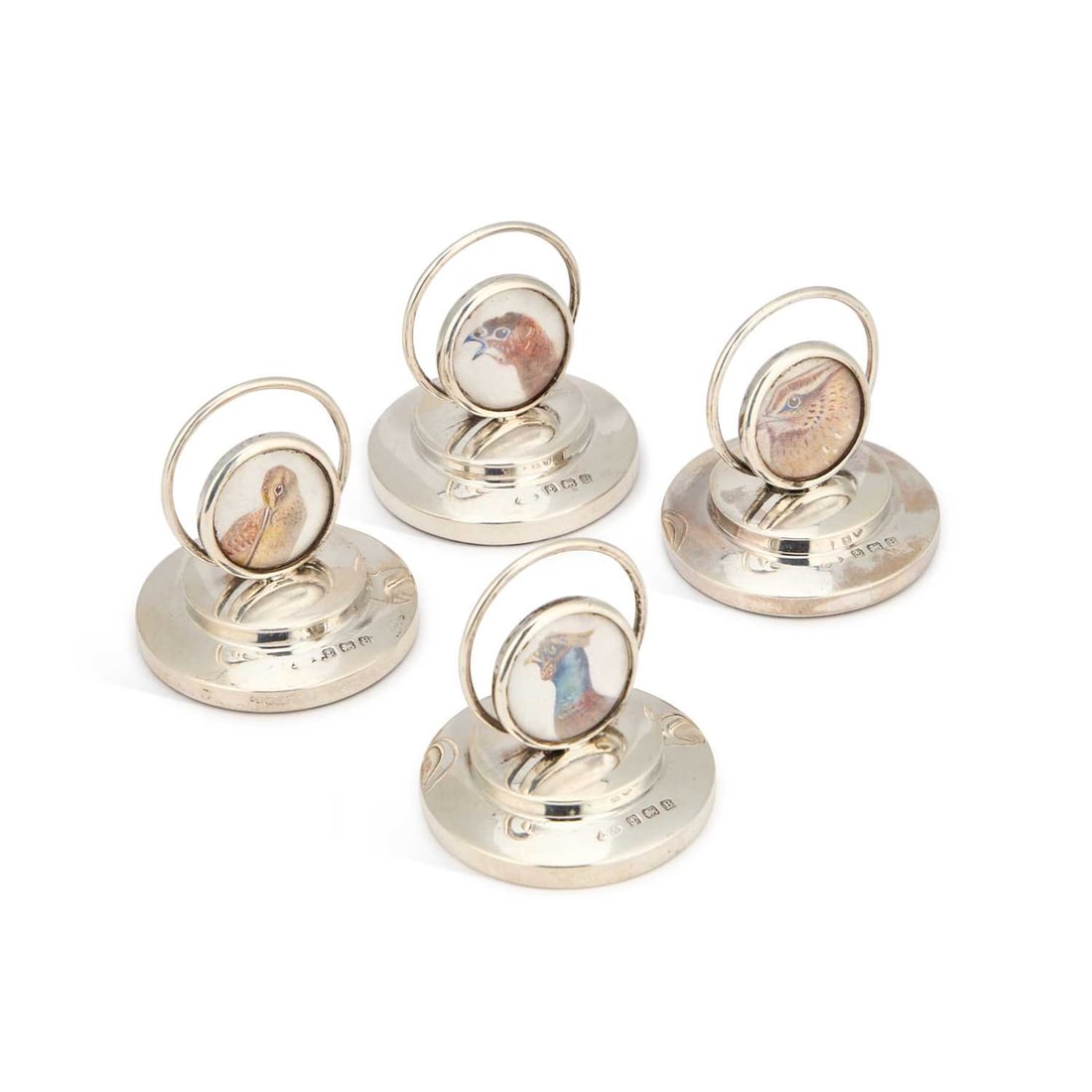 A SET OF FOUR GEORGE V SILVER MENU HOLDERS: A SET OF FOUR GEORGE V SILVER MENU HOLDERS by Adie Brothers Ltd, Birmingham 1926, each with a circular back watercolour painted beneath convex glass with a different profile of a game bird, raised on 