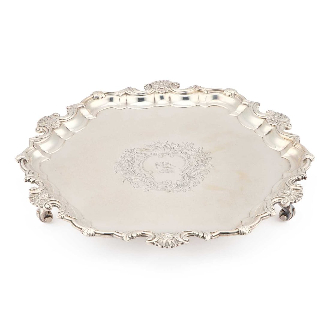 A GEORGE II SILVER SALVER: A GEORGE II SILVER SALVER by George Wickes, London 1742, of shaped hexagonal form with three scroll-form feet, the rim cast with shells and scrolls, engraved with a crest within a Rocaille cartouche.