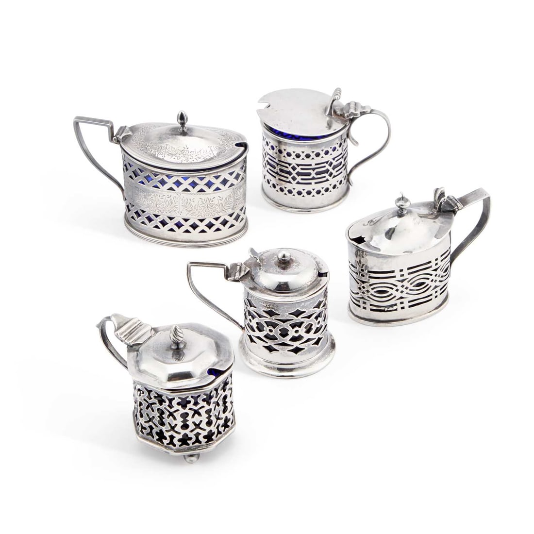 A GROUP OF FIVE PIERCED SILVER MUSTARD POTS: A GROUP OF FIVE PIERCED SILVER MUSTARD POTS including a Victorian oval mustard pot by Florence Warden, Chester 1895, and a variety of other pierced silver examples, each with well-fitted blue glass li