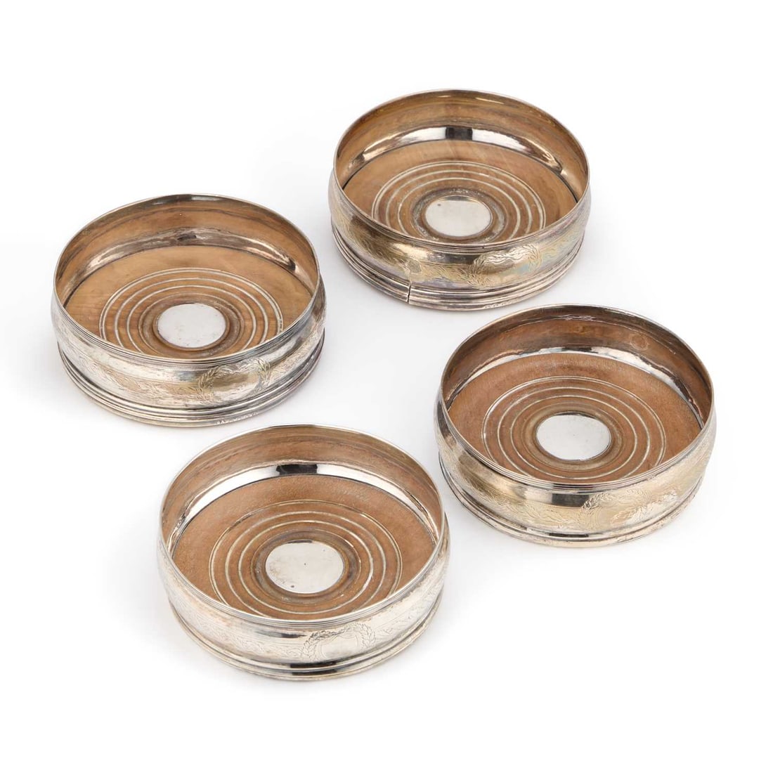 A SET OF FOUR GEORGE III SILVER WINE COASTERS: A SET OF FOUR GEORGE III SILVER WINE COASTERS probably by Stephen Adams, London 1800 and 1808, each circular with a reeded rim and foliate engraved rounded sides, each turned wooden base centred by an