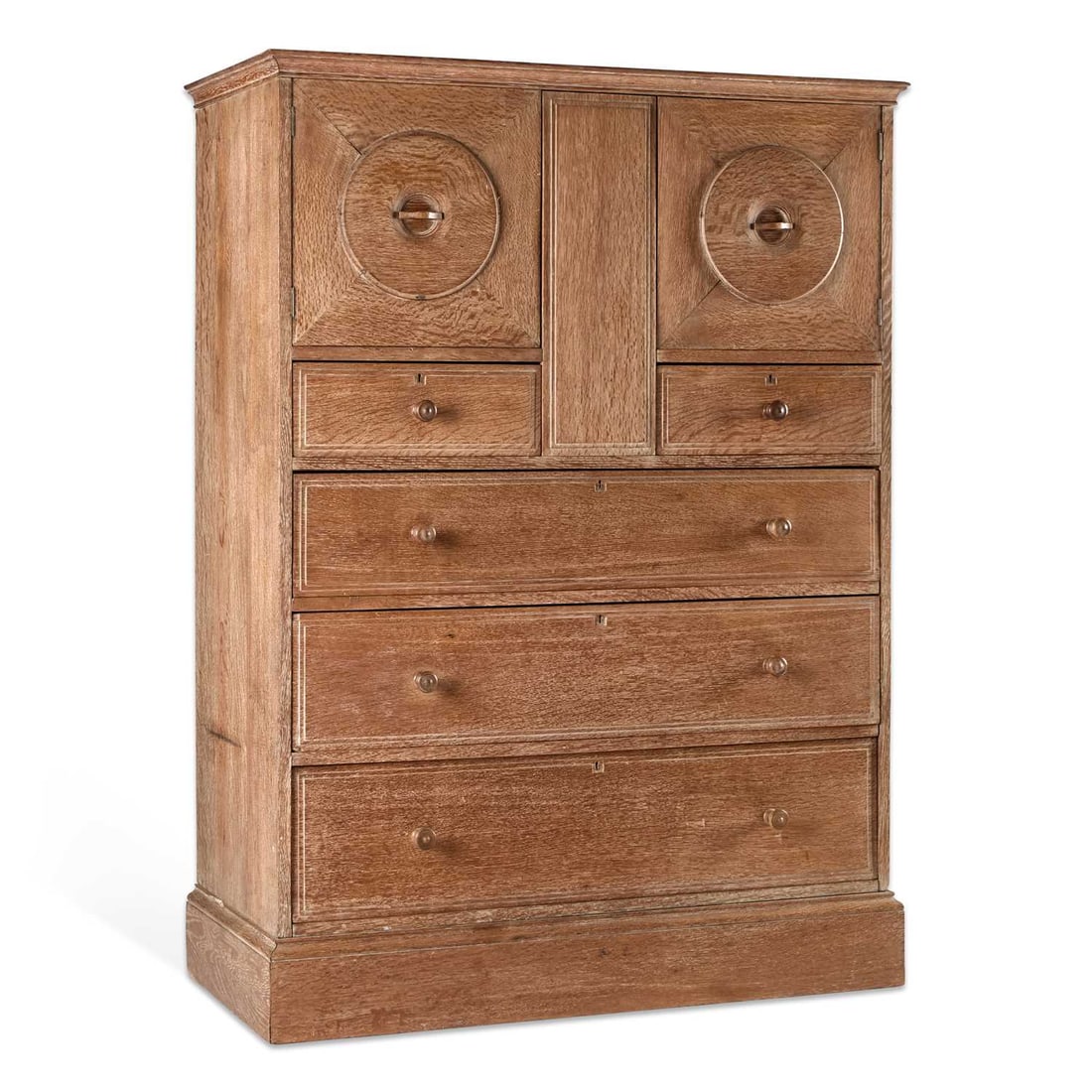AMBROSE HEAL FOR HEAL'S, A LIMED OAK 'OWL' CABINET EARLY 20TH CENTURY: AMBROSE HEAL FOR HEAL'S, A LIMED OAK 'OWL' CABINET EARLY 20TH CENTURY with a pair of square doors centred by circular roundels, above a pair of short drawers with three long graduated drawers with tur