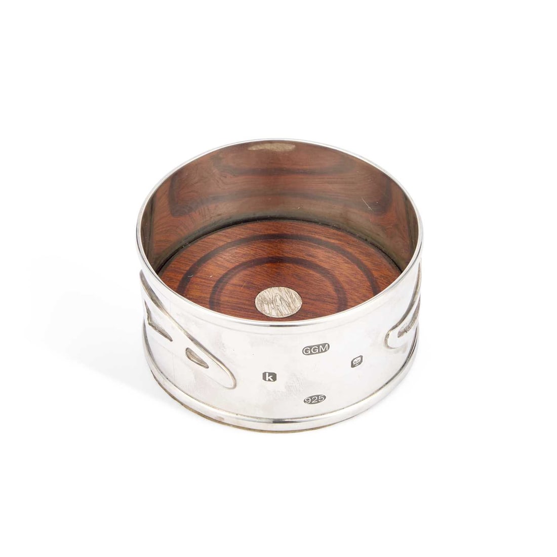 AN ELIZABETH II SILVER WINE COASTER: AN ELIZABETH II SILVER WINE COASTER maker GGM, London 2009, of circular form, the sides with three abstract motifs enclosing a hardwood base. 9.5cm diameter