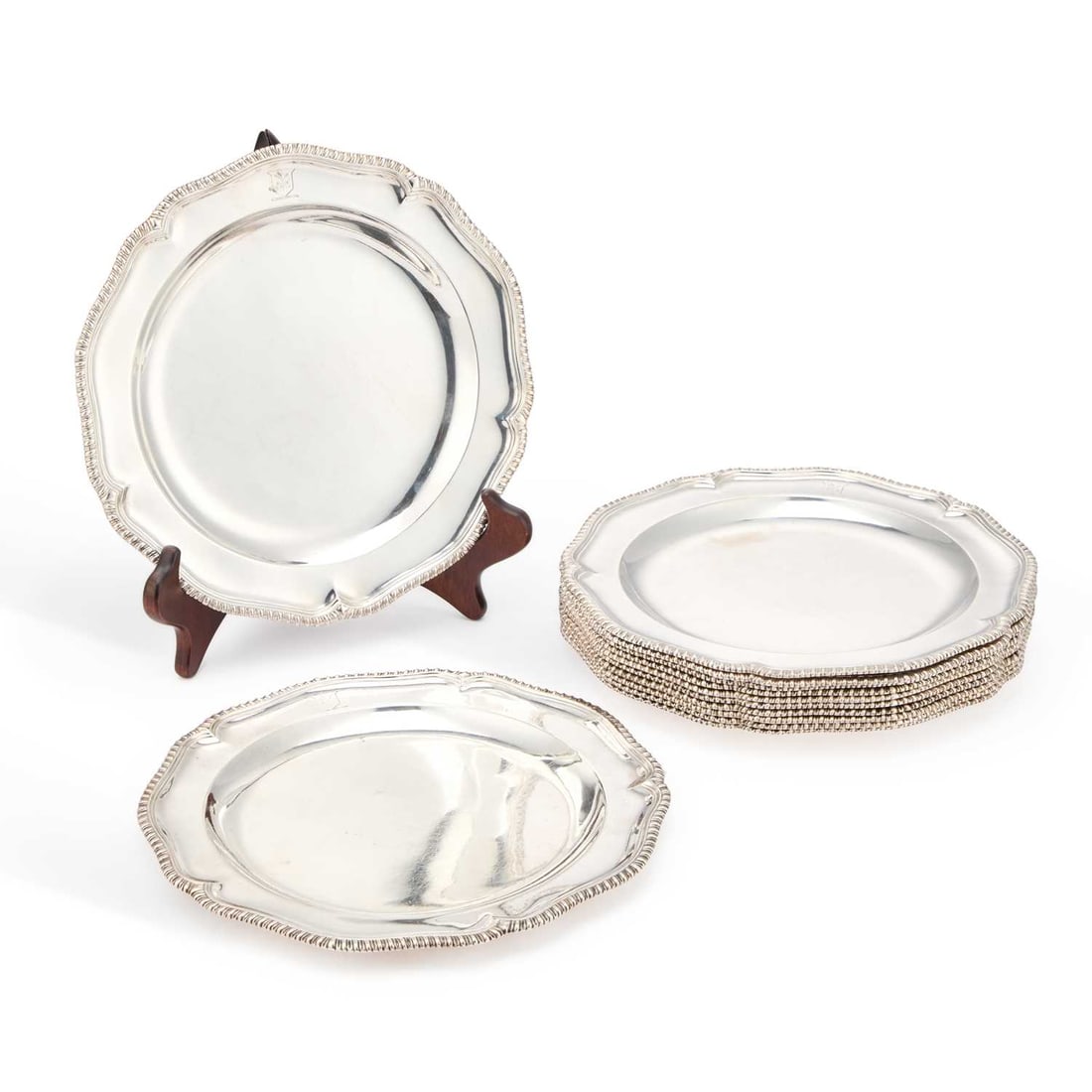 A SET OF TWELVE GEORGE III SILVER DINNER PLATES: A SET OF TWELVE GEORGE III SILVER DINNER PLATES probably by John King, London 1764, of cusped circular form with gadrooned edges, engraved with crests, scratch-weights and set numbers. (12) 24cm diame