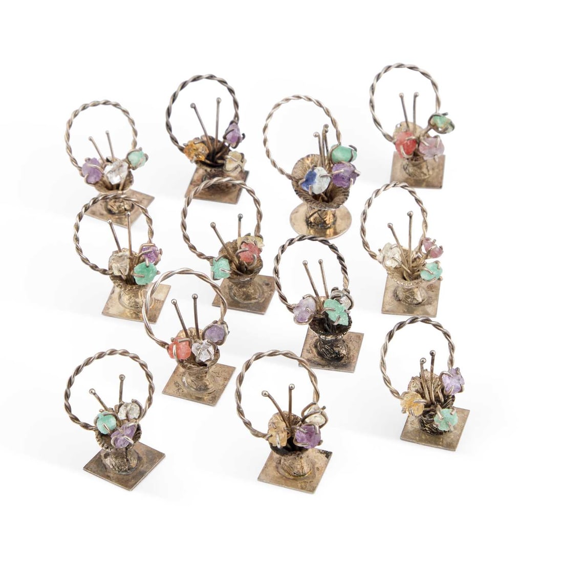 A SET OF TWELVE SILVER AND 'JEWELLED' MENU HOLDERS: A SET OF TWELVE SILVER AND 'JEWELLED' MENU HOLDERS 833 standard, each indistinctly marked and modelled as a basket of flowers. (12) Tallest 3cm, 2.9 troy ounces
