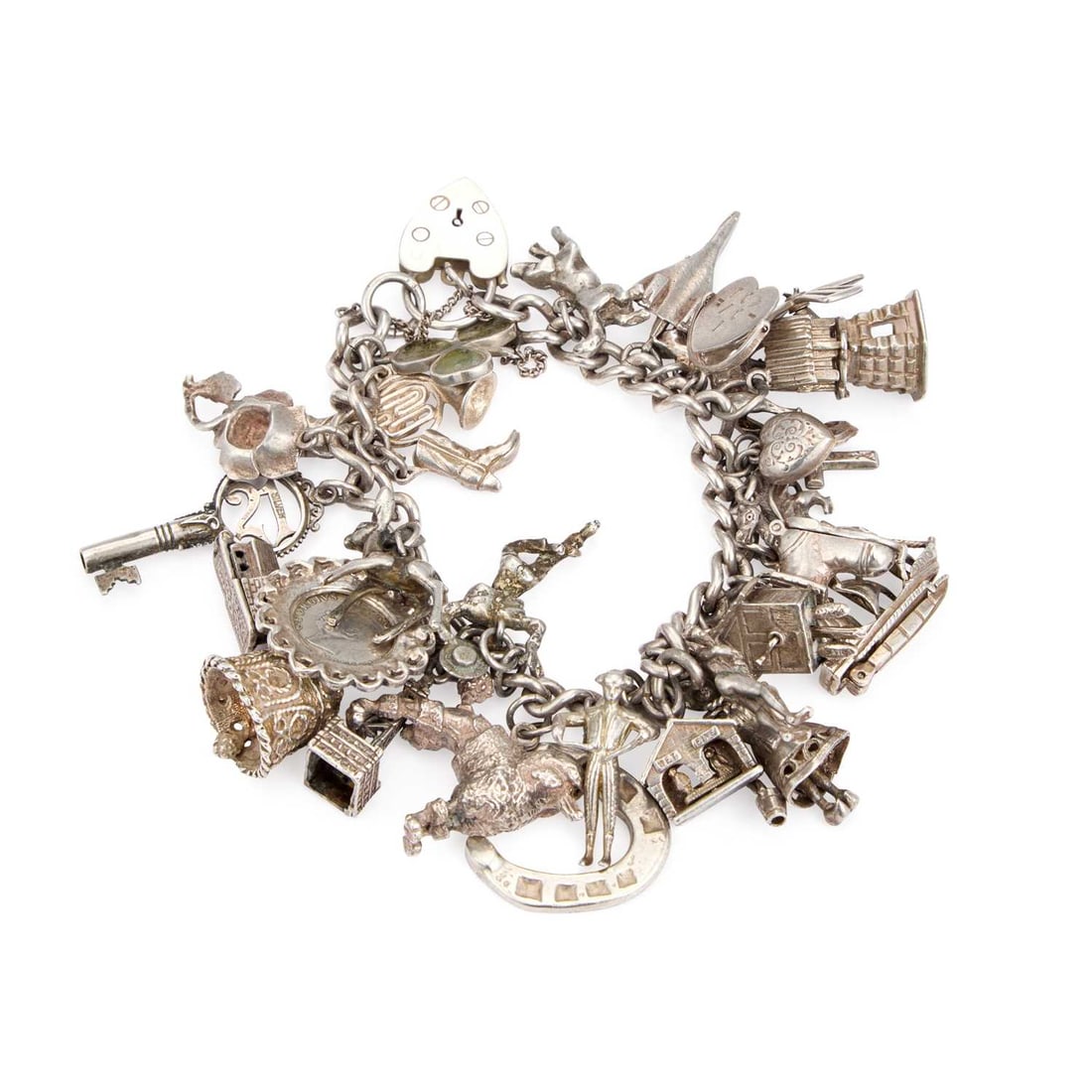 A SILVER CHARM BRACELET: A SILVER CHARM BRACELET with a heart padlock closure, the chain adorned with various charms including a boxer dog, French horn, Babycham deer, a Connemara marble-set shamrock, etc. 117 grams
