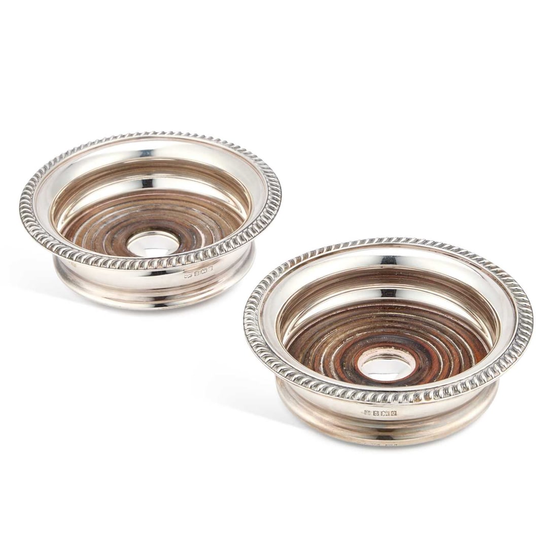 A NEAR PAIR OF ELIZABETH II SILVER WINE COASTERS: A NEAR PAIR OF ELIZABETH II SILVER WINE COASTERS by Mappin & Webb Ltd and Barker Ellis Silver Co, Birmingham 1967 and 1965, in George III style, with gadrooned rims and turned wooden bases. (2) 14