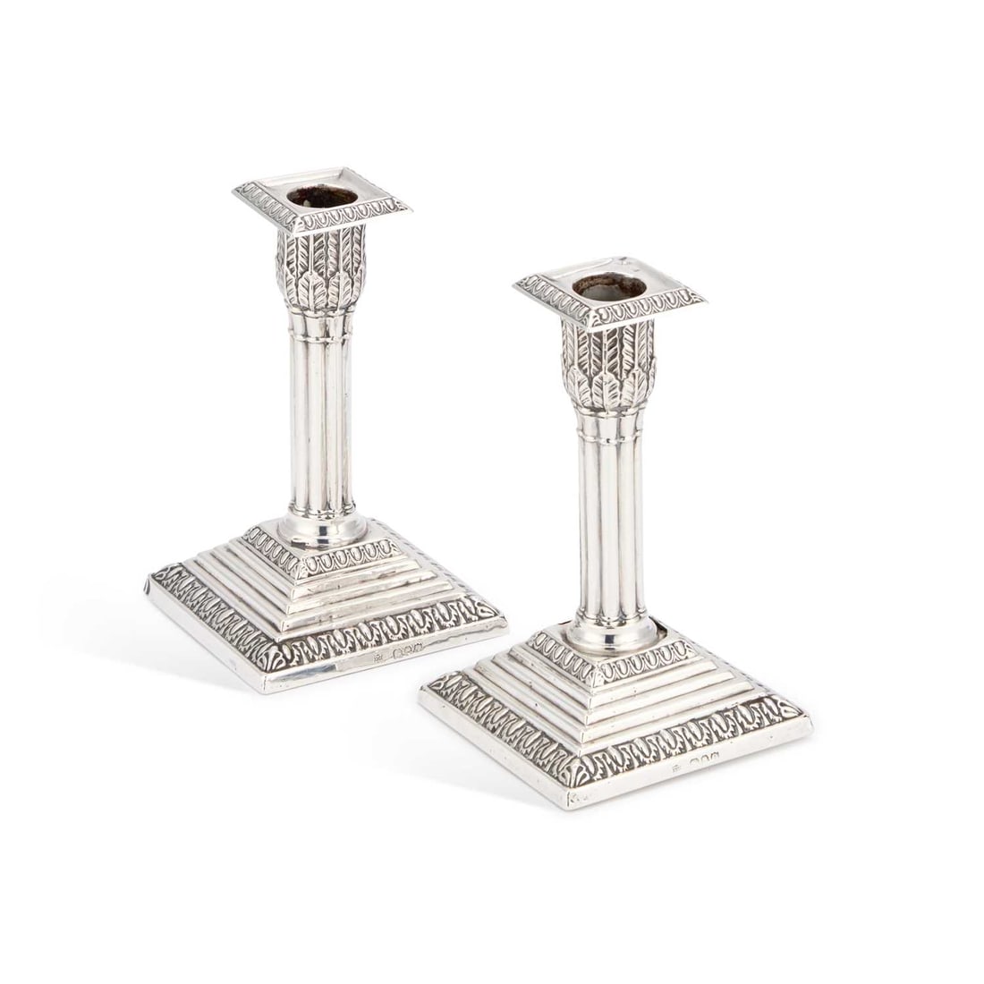 A PAIR OF VICTORIAN SILVER CANDLESTICKS: A PAIR OF VICTORIAN SILVER CANDLESTICKS by Edward Hutton, London 1891, each with a cluster-column stem rising from a stepped square base with a leaf-chased border, loaded. (2) 14cm high