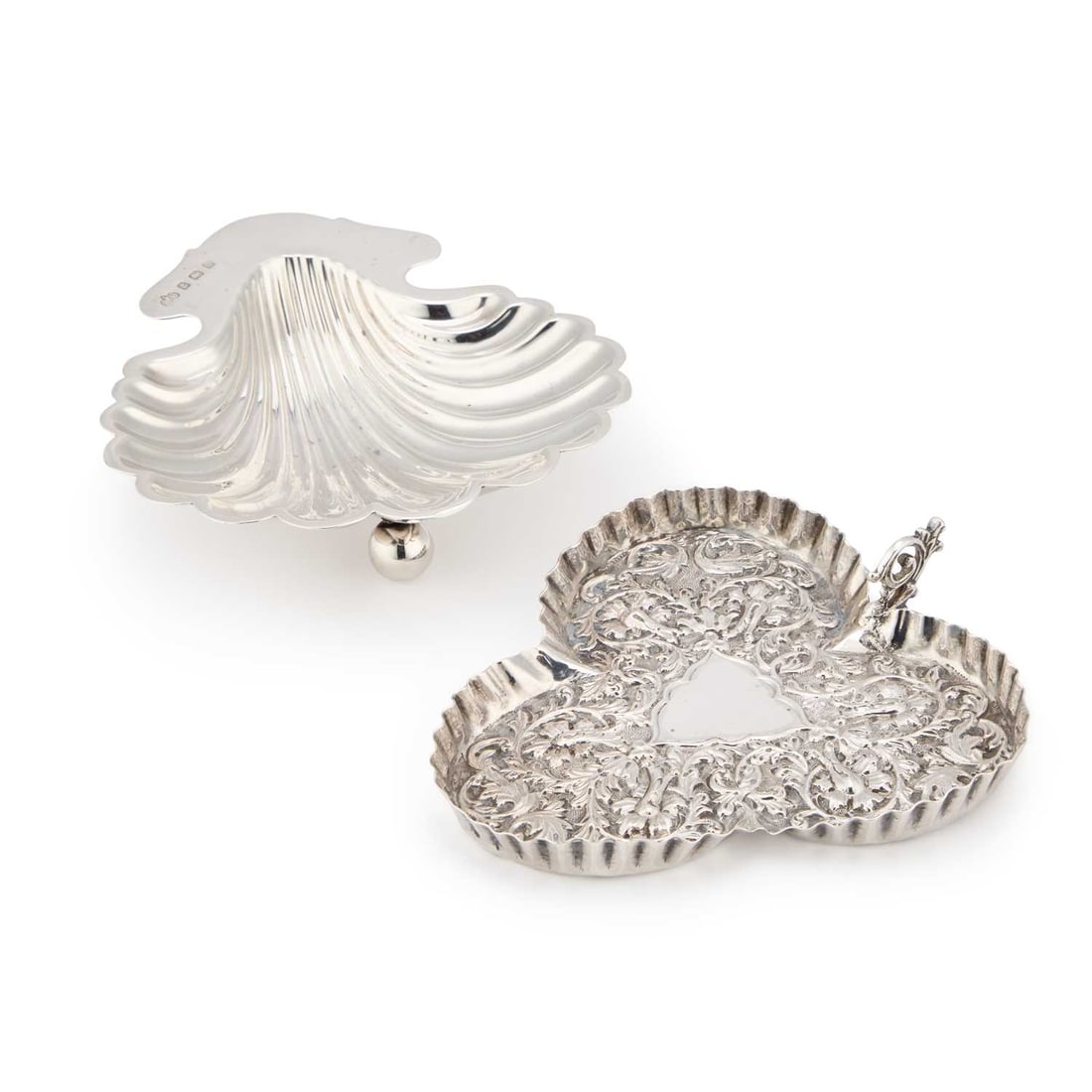 TWO SILVER DISHES: TWO SILVER DISHES the first a Victorian silver pin tray by Charles Stuart Harris, London 1887, the trefoil dish with a shaped edge, repoussé with scrolling foliage to a stippled ground, a vacant tria