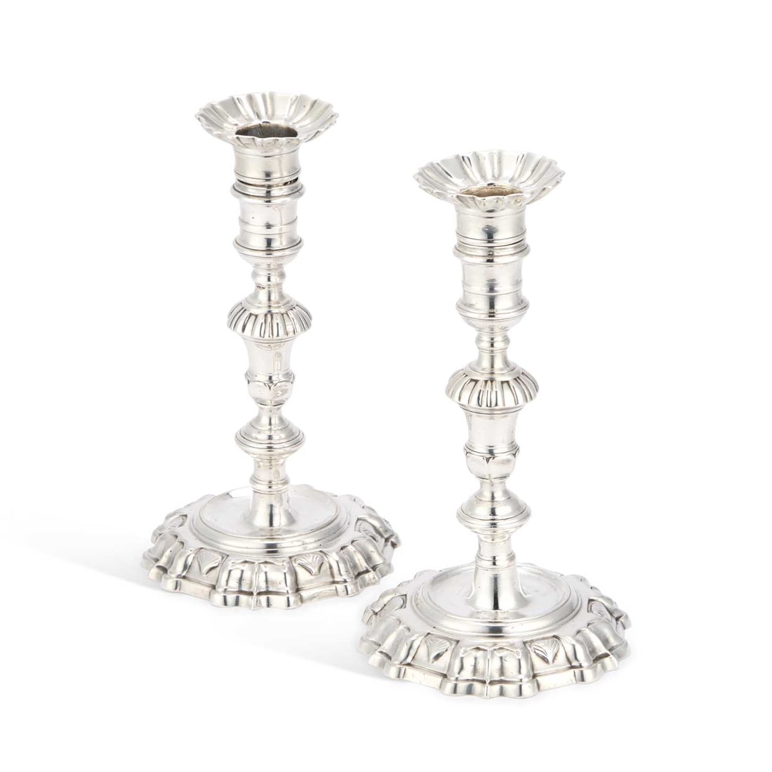 A PAIR OF GEORGE II CAST SILVER CANDLESTICKS: A PAIR OF GEORGE II CAST SILVER CANDLESTICKS by James Gould, London 1737, the knopped stems with reeded and reel decoration, the shaped circular foot of each with cast shell detail, with scalloped cir