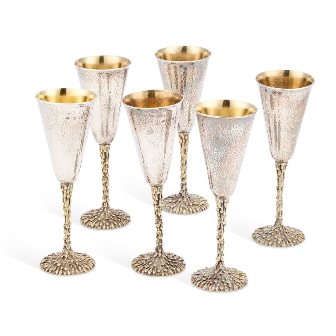 A SET OF SIX ELIZABETH II PARCEL-GILT SILVER CHAMPAGNE FLUTES: A SET OF SIX ELIZABETH II PARCEL-GILT SILVER CHAMPAGNE FLUTES by Stuart Devlin, London 1975, each with a hammered tapering bowl on a stem simulating melting candle wax. (6) 19cm high, 39.9 troy ounces