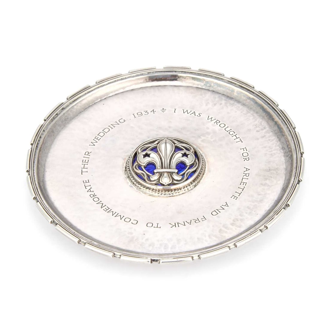 AN ARTS AND CRAFTS SILVER AND ENAMEL DISH: AN ARTS AND CRAFTS SILVER AND ENAMEL DISH by Omar Ramsden, London 1933, of circular form with piecrust rim and centred with a blue enamel fleur-de-lys roundel, engraved COMMEMORATE THEIR WEDDING 1934 