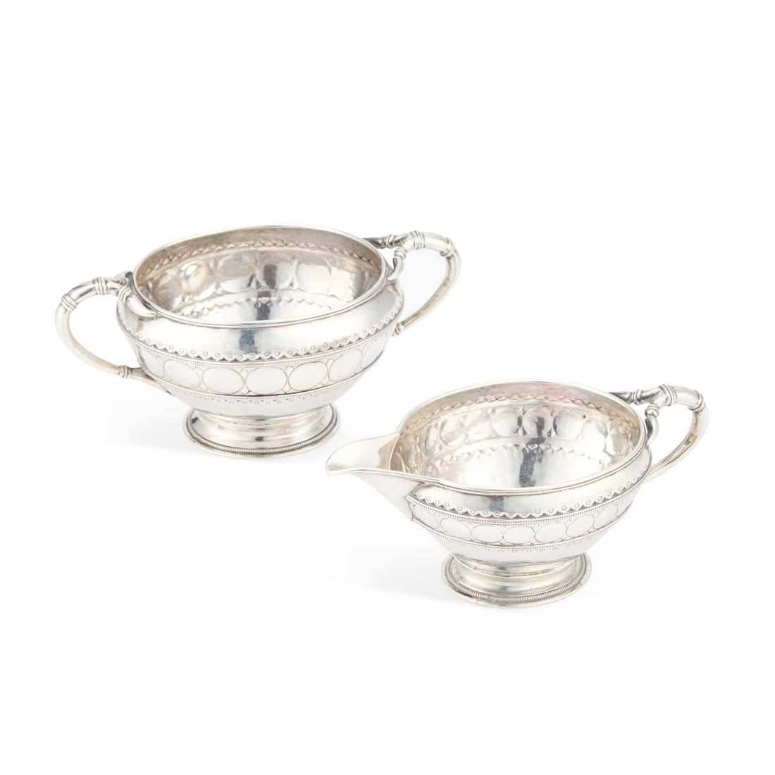 AN ARTS AND CRAFTS SILVER CREAM JUG AND SUGAR BOWL: AN ARTS AND CRAFTS SILVER CREAM JUG AND SUGAR BOWL by Liberty & Co Ltd, Birmingham 1910, each of oval form with bifurcated handle(s) and chased with a band of roundels and arrowheads, further deco
