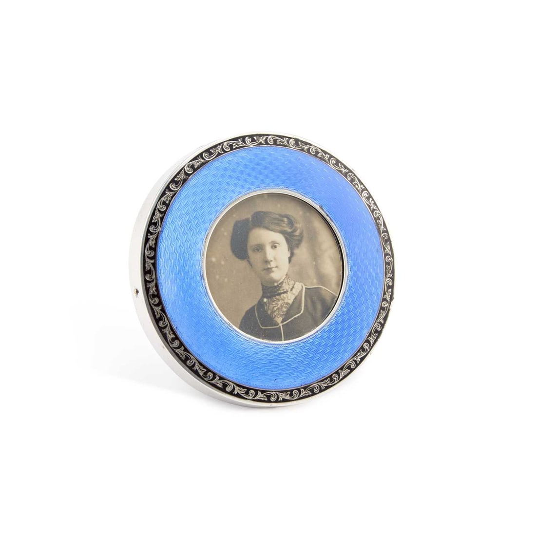 A GEORGE V SILVER AND ENAMEL PHOTOGRAPH FRAME: A GEORGE V SILVER AND ENAMEL PHOTOGRAPH FRAME by Henry Matthews, Birmingham 1924, circular form, with blue guilloché enamel and a black enamelled scrolling foliate border, easel back, (a/f). 8.3cm di