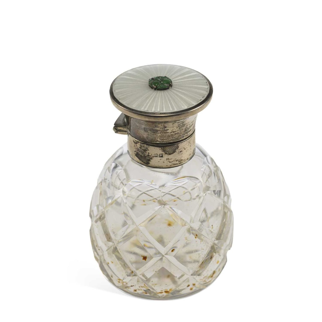AN ELIZABETH II SILVER AND ENAMEL-MOUNTED CUT-GLASS SCENT BOTTLE: AN ELIZABETH II SILVER AND ENAMEL-MOUNTED CUT-GLASS SCENT BOTTLE by Henry Clifford Davis, Birmingham 1955, the white guilloché enamel top set with a carved green jade stone. 10.7cm high