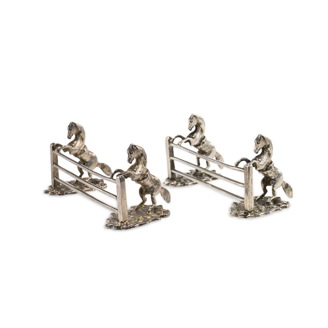 A PAIR OF ELIZABETH II NOVELTY SILVER EQUESTRIAN THEME KNIFE RESTS: A PAIR OF ELIZABETH II NOVELTY SILVER EQUESTRIAN THEME KNIFE RESTS by S. J. Rose & Son, Birmingham 1970, each in the form of a pair of horse leaping over a jump on a naturalistic base. (2) 9.5cm