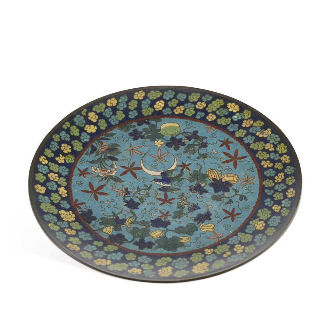 A JAPANESE CLOISONNÉ PLAQUE MEIJI PERIOD: A JAPANESE CLOISONNÉ PLAQUE MEIJI PERIOD enamelled with a bird flying amongst fruiting and flowering plants, before a crescent moon, within a border of stylised flowerheads. 30.5cm diameter
