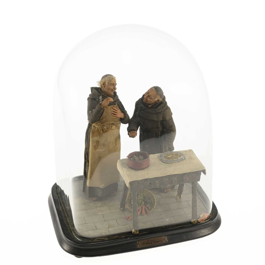 A WAX AND MIXED-MEDIA FIGURAL DIORAMA ‘THE FIRST TASTE’: A WAX AND MIXED-MEDIA FIGURAL DIORAMA ‘THE FIRST TASTE’ modelled as two jovial friars standing beside a table laid with food, raised on an ebonised rectangular base with an applied title plaque an