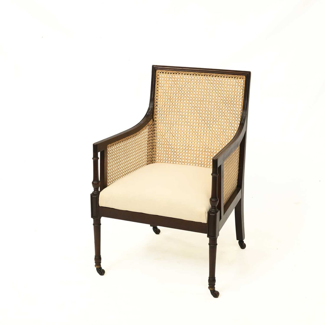 A 19TH CENTURY MAHOGANY CANED BERGÈRE ARMCHAIR: A 19TH CENTURY MAHOGANY CANED BERGERE ARMCHAIR the rectangular cane-filled back above swept arms and cane-filled sides, with a cream upholstered seat, raised on turned front legs and square rear