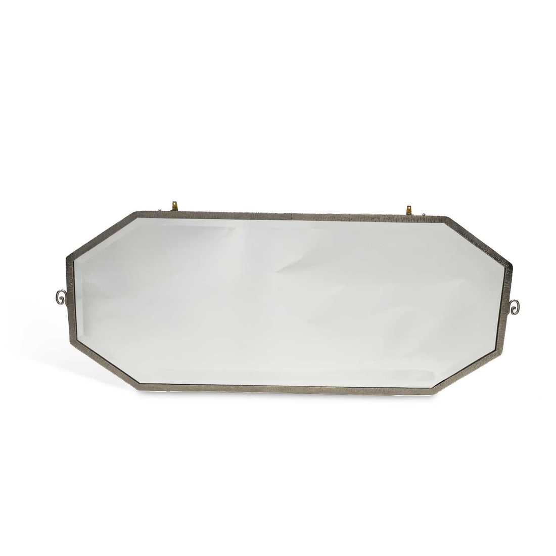 V A MID-20TH CENTURY SILVERED-METAL FRAMED WALL MIRROR: V A MID-20TH CENTURY SILVERED-METAL FRAMED WALL MIRROR the long bevelled octagonal plate within a narrow textured frame, with scroll terminals to the sides. 52cm high, 131cm wide