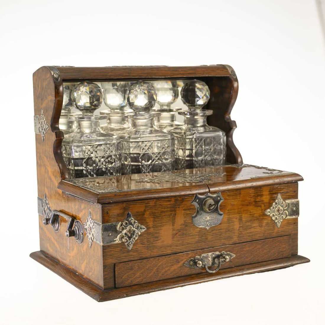 A LATE VICTORIAN OAK, SILVER-PLATED AND CUT-GLASS THREE-BOTTLE TANTALUS: A LATE VICTORIAN OAK, SILVER-PLATED AND CUT-GLASS THREE-BOTTLE TANTALUS the mirrored superstructure fitted with three square cut-glass decanters and faceted ball stoppers, above twin hinged compartmen