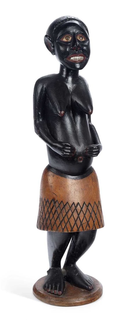 AN AFRICAN CARVED AND PAINTED WOOD FIGURE OF A WOMAN: standing with her hands to a swollen belly, the body ebonised, with inset eyes and painted lips and eye rims, the hair worked with punched decoration, wearing a skirt incised with a lattice pattern, o