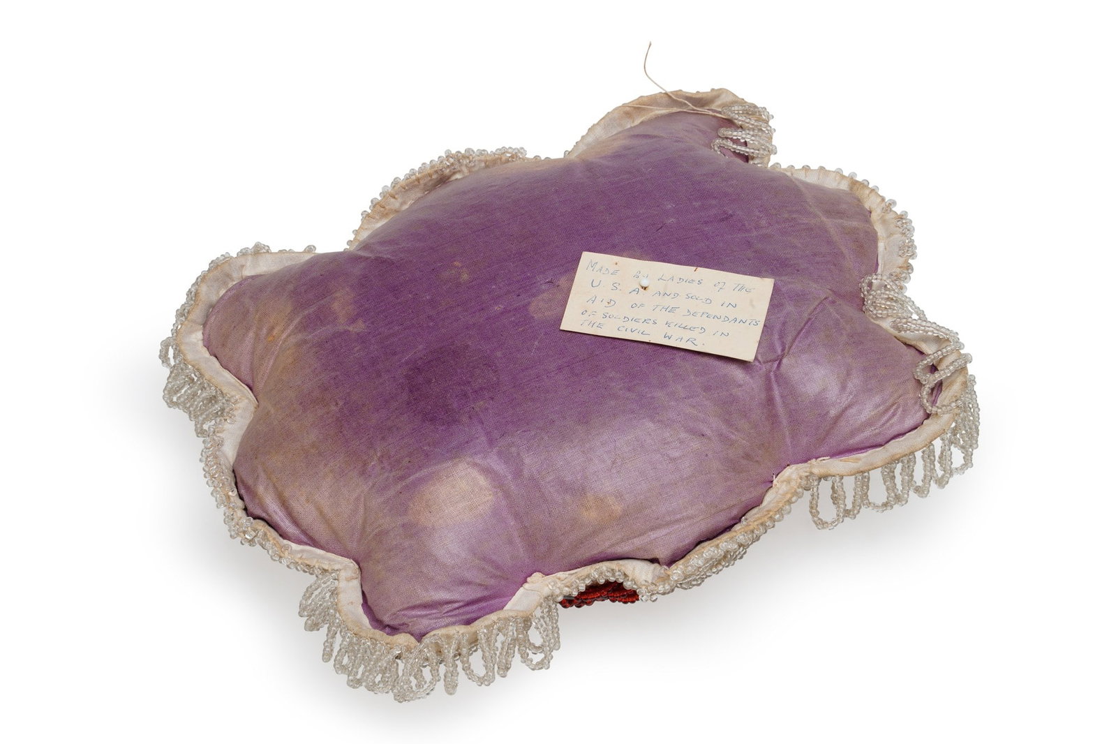 AN IROQUOIS BEADWORK PINCUSHION 19TH CENTURY: of shaped cushion form, the purple velvet face worked in clear and coloured glass beads with a dove among flowering branches, within a raised petal border of linked swags, the reverse with an old