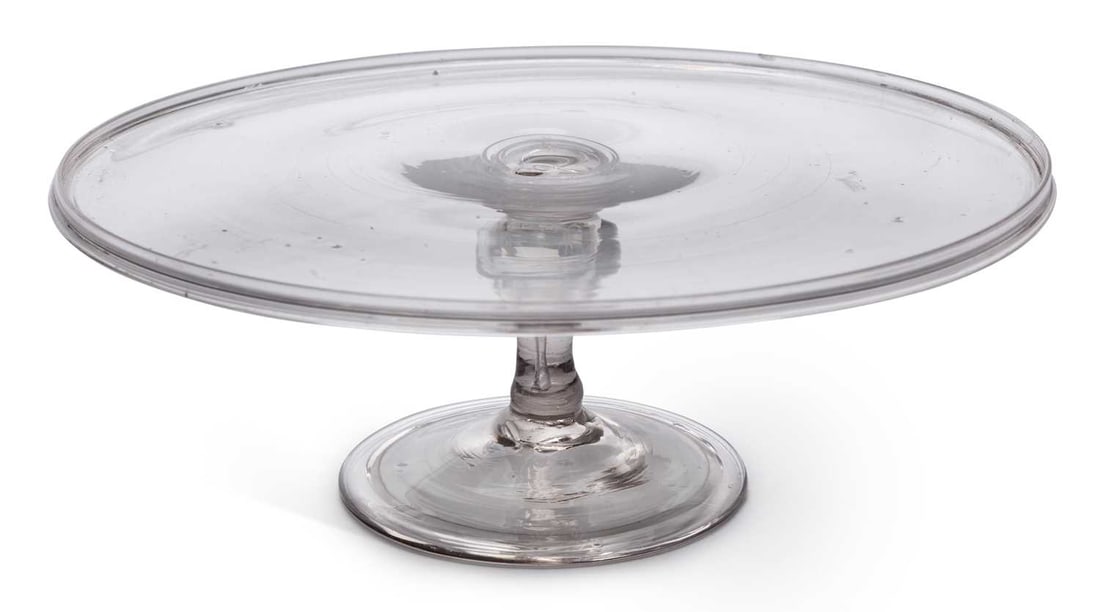 A GLASS TAZZA 18TH CENTURY: the dished top with a folded rim, on a short plain stem and domed folded foot. 28cm diameter, 10.5cm high