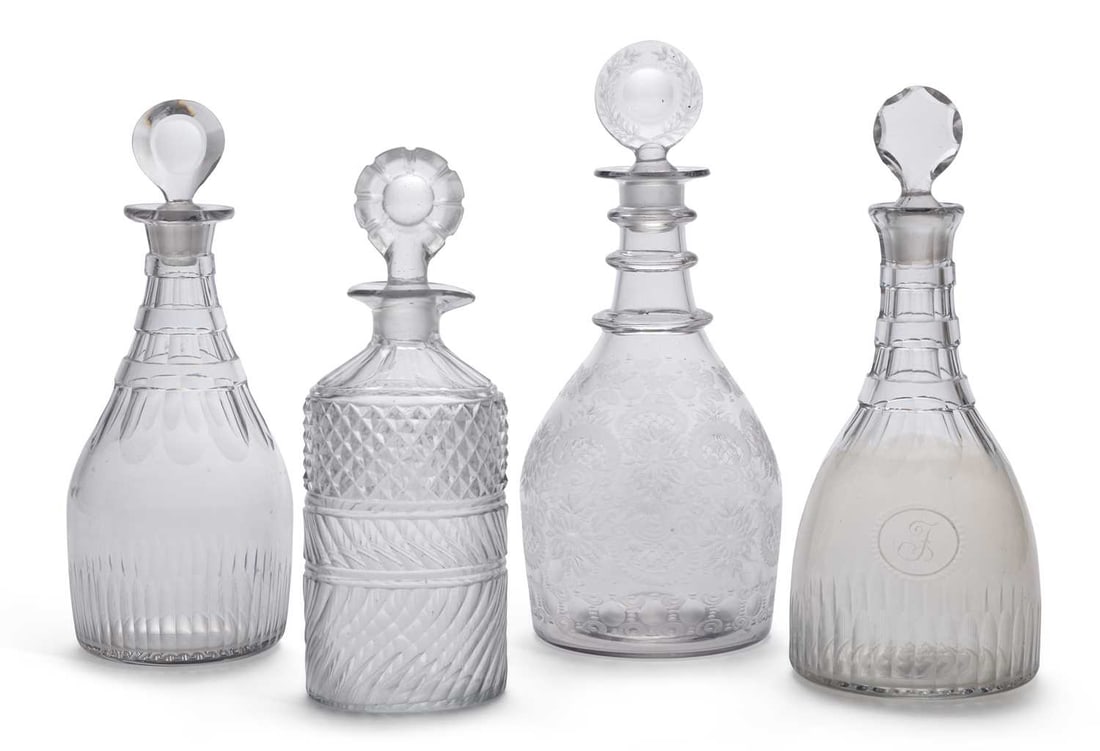 FOUR CUT-GLASS DECANTERS 18TH AND 19TH CENTURY: comprising one with slice cut neck rings and a target stopper; one cut with diamonds and swirled flutes; one engraved with fruiting vine with a wheel cut stopper; and one with a moulded medallion init