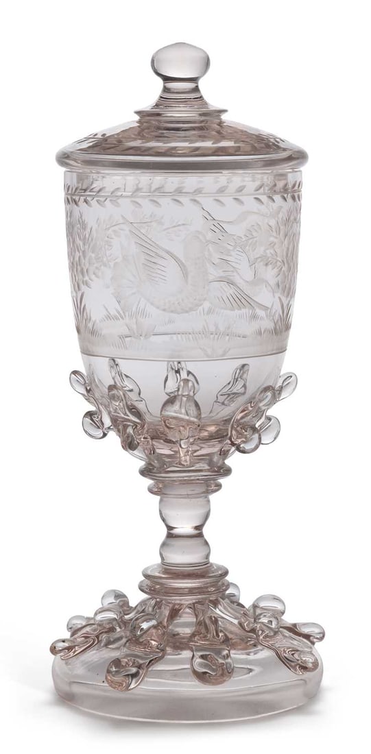A CONTINENTAL ENGRAVED GLASS COVERED GOBLET 19TH CENTURY: engraved with a bird amongst foliage in a landscape within laurel borders, the lower bowl and foot applied with raspberry prunts and trailing, raised on a knopped stem, the domed cover with a ball fin