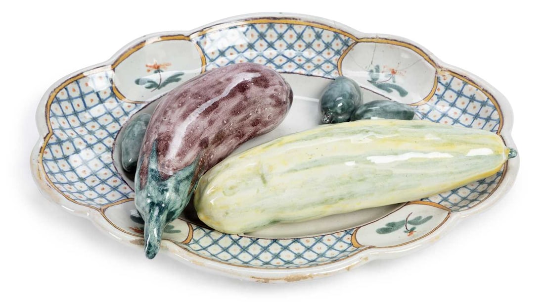 A FRENCH FAIENCE TROMPE L'OEIL DISH CIRCA 1800: the oval-shaped dish applied with a group of vegetables, within a polychrome border. 30.5cm wide