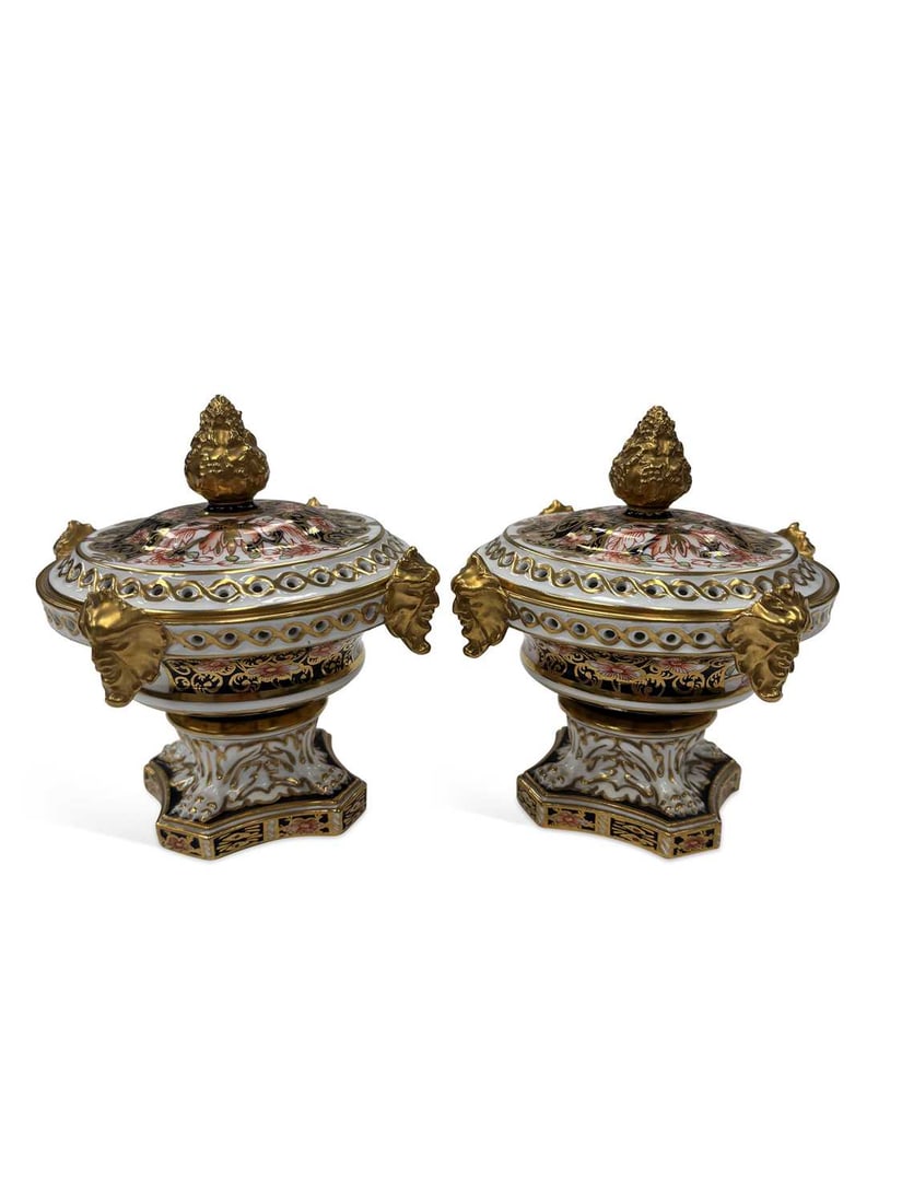 A PAIR OF ROYAL CROWN DERBY IMARI POT POURRI VASES AND COVERS EARLY 20TH CENTURY: each of urn form with gilt mask handles, the pierced domed cover with an artichoke finial, painted in the Imari palette in underglaze blue, iron-red and gilt, raised on a shaped square base, printed