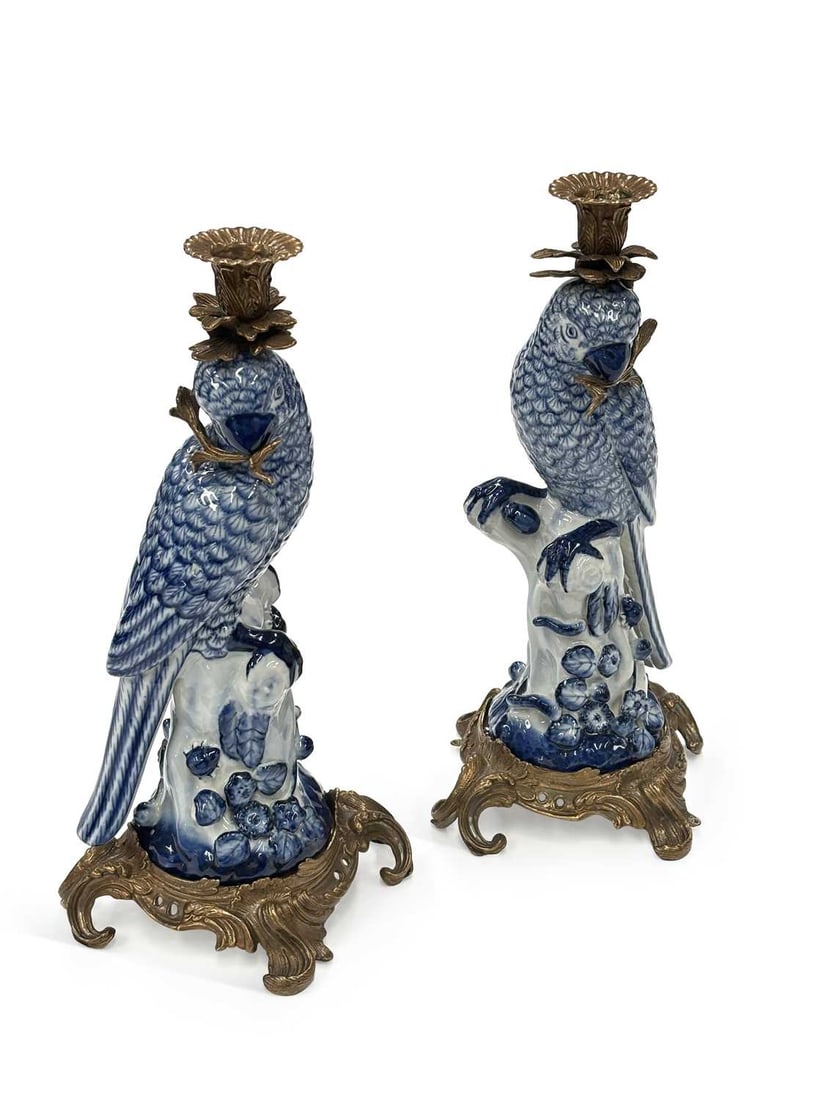 A PAIR OF BRASS-MOUNTED BLUE AND WHITE PORCELAIN PARROT CANDLESTICKS: each modelled as a parrot perched upon a flowering tree stump, painted in underglaze blue with scale pattern plumage, the foliate cast candle nozzle and drip pan rising from the head, on a pierced