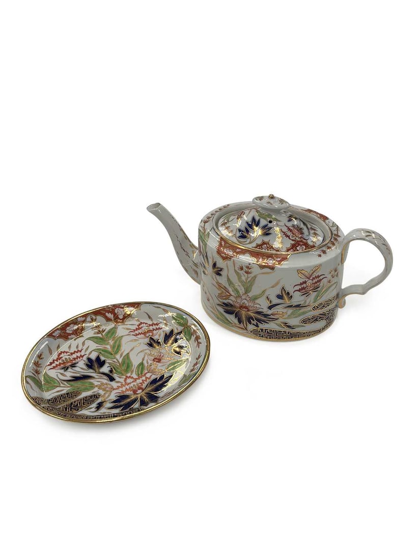 A COALPORT PORCELAIN TEAPOT, COVER AND STAND CIRCA 1820: of drum form with a loop handle and straight spout, the domed cover with a knop finial, painted in the Imari palette in cobalt blue, iron-red, green and gilt with flowering plants beneath a panelled