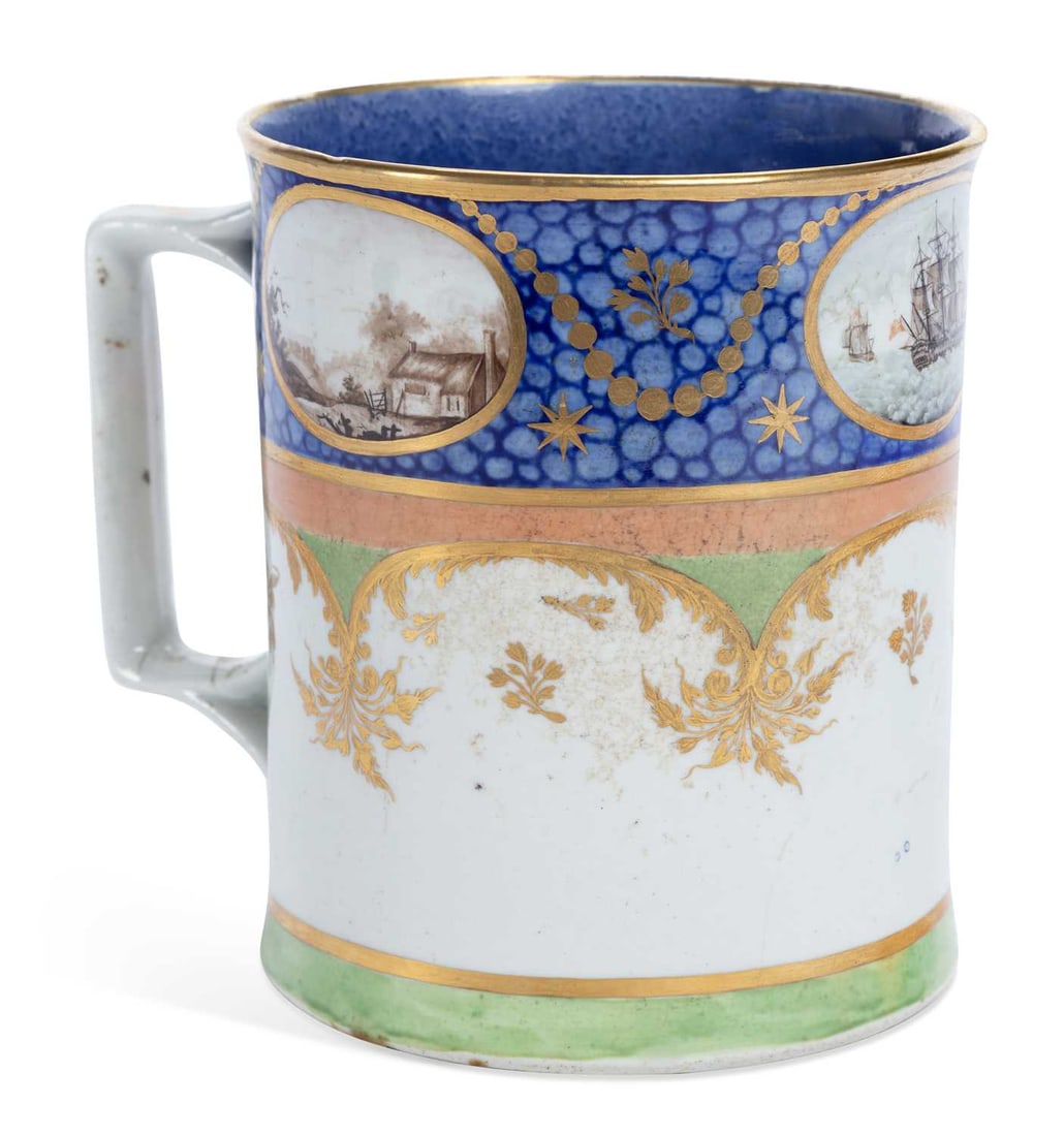 AN ENGLISH PORCELAIN MUG CIRCA 1800: painted with oval panels containing scenes of ships at sea and rural landscapes, suspended from gilt swags, on a fond cailloute blue ground. 13.5cm high