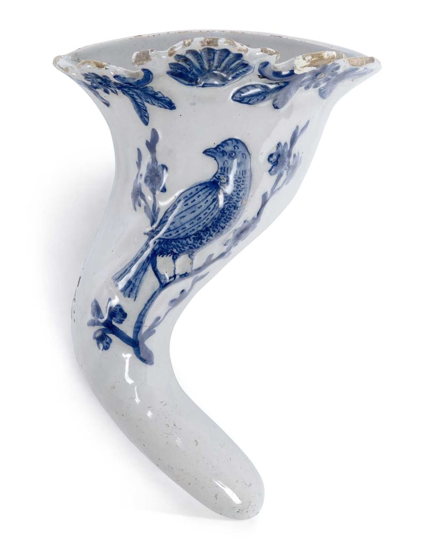 A LIVERPOOL DELFT WALL POCKET CIRCA 1760: the spiral shaped wall pocket with a bird perched on a branch, beneath a shell and leaf moulded rim, painted in underglaze blue, having twin piercings to the reverse for suspension. 22cm high