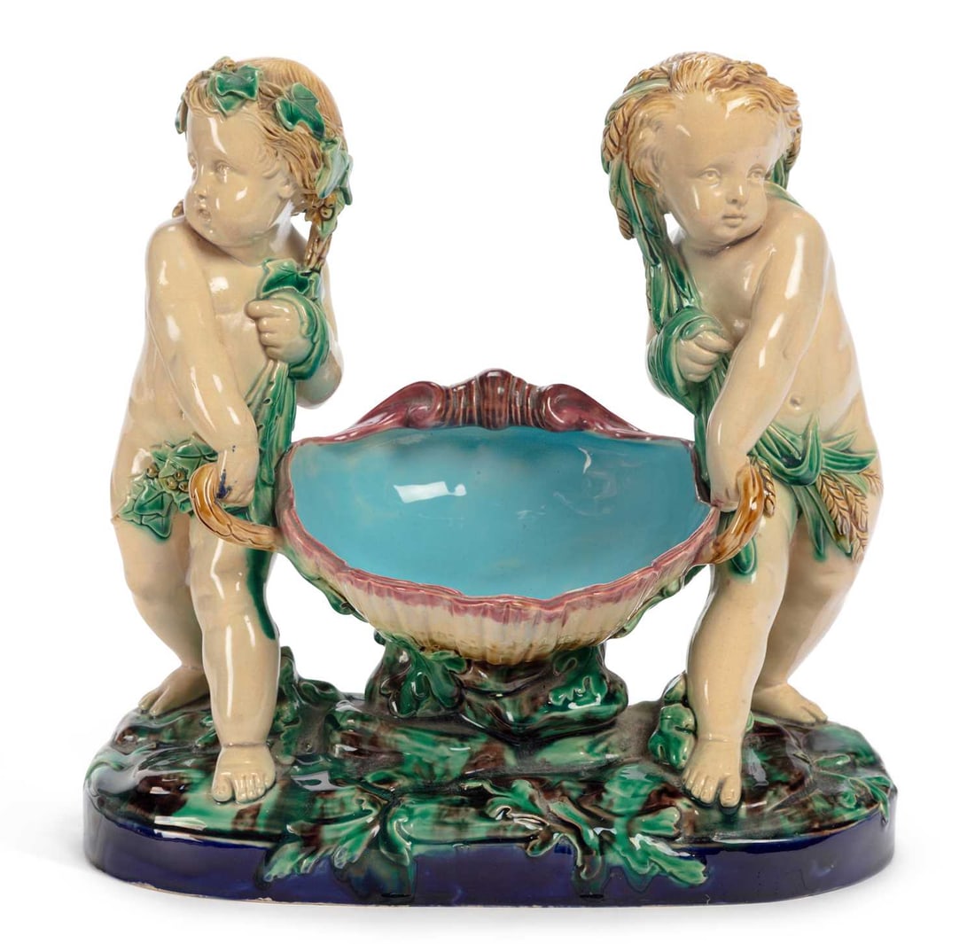 A MINTON MAJOLICA CHERUBS BASKET DATED 1868: modelled as two cherubs carrying a large shell, impressed factory marks and date code for 1868. 28.5cm wide Surface dirt but no visible cracks, repairs or losses