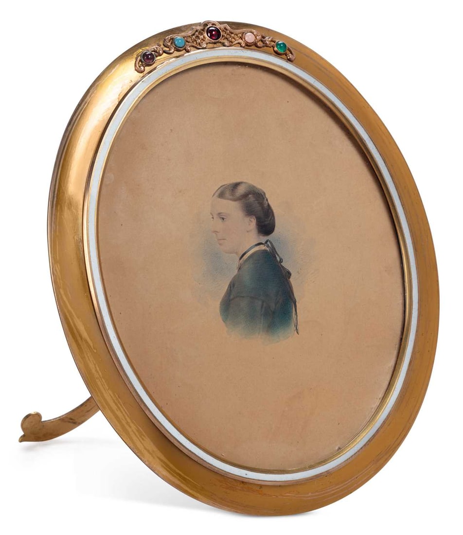 AN ASPREY GILT-BRASS EASEL FRAME LATE 19TH CENTURY: the oval aperture within a moulded surround, the cresting cast with foliate scrolls and set with gems, with a pierced scroll easel support, the reverse engraved Asprey. 166. Bond St & 22. Albemarle St