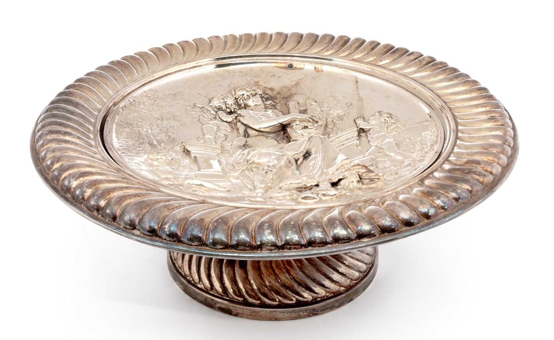 A SILVER-PLATED TAZZA OR PEDESTAL DISH: of circular form, decorated in relief with a classical scene of a female figure playing a lyre with winged cherub attendants, within a gadrooned border. 29.2cm diameter