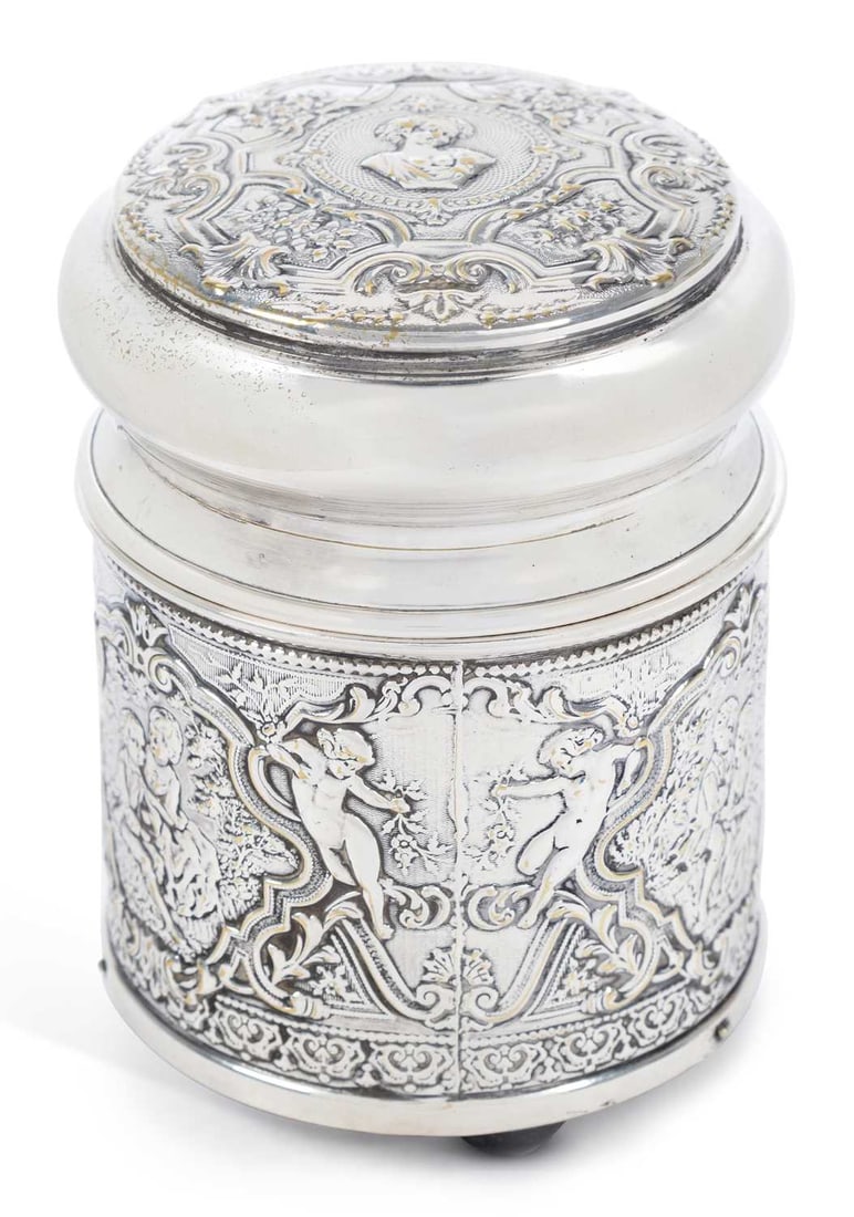 A FRENCH SILVER-PLATED MUSICAL JAR AND COVER: of circular form, repousse decorated with panels of courting couples, baskets of flowers and cherubs, fitted with a musical movement, the pull-off cover revealing a cut-glass liner, stamped 'Made in