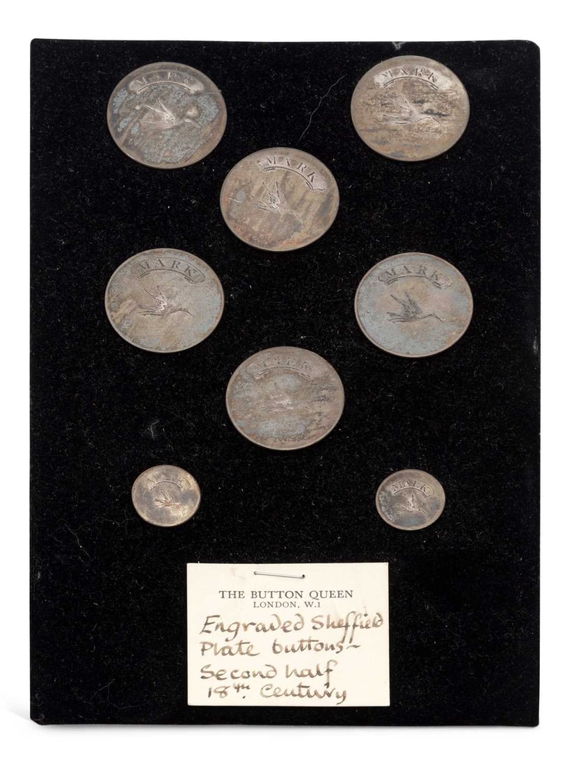 A CARD OF SHEFFIELD PLATE BUTTONS: each engraved with a bird in flight beneath a ribbon inscribed MARK, comprising six larger and two smaller, mounted on a card from The Button Queen, London, described as second half 18th Century. (8)