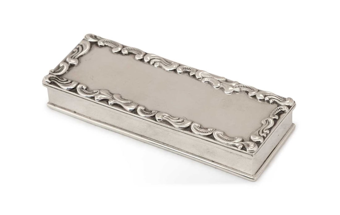 AN AMERICAN STERLING SILVER STAMP BOX: by J. E. Caldwell & Co., of rectangular form, the hinged cover decorated with a cast scroll border, opening to a triple compartment, marked to base. 9.5cm by 3.5cm by 1.5cm, 2.7 troy ounces Good
