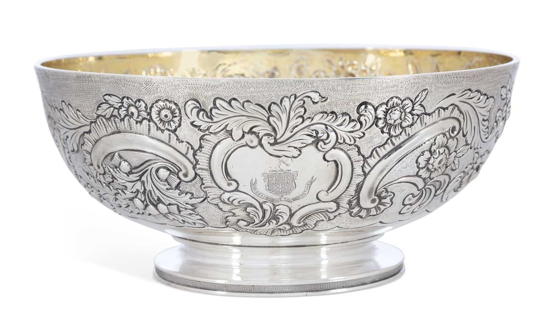 A GEORGE III SCOTTISH SILVER BOWL: by George McHattie, Edinburgh 1817, of circular form, chased with flowerheads and C-scrolls on a textured ground, engraved with a coat of arms to a cartouche, raised on a reeded pedestal foot, gilded 