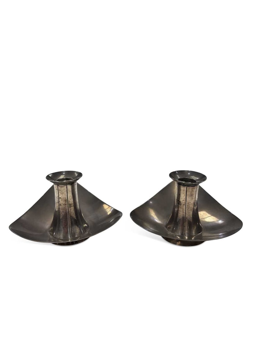 A PAIR OF ELIZABETH II MODERNIST SILVER CANDLESTICKS: by Nayler Brothers, London 1957, of curved triangular form, with waisted column on a spreading circular foot. (2) 5cm high, 4.8 troy ounces gross Stand well, tarnish and light surface scratches.